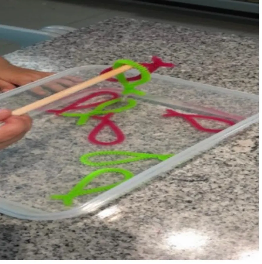 Manos pescan figuras de limpiapipas en una charola con un palito
